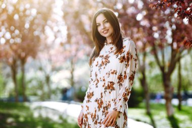 Çiçekli güzel elbiseli çekici bir kadının portresi bahar günü çiçek açan yeşil bahçenin tadını çıkarıyor. Moda ve tarz kavramı.