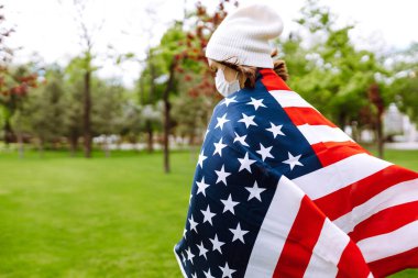 Amerikan bayrağı taşıyan koruyucu maskeli genç bir kız. Amerika 'nın Bağımsızlık Günü. 4 Temmuz. Amerika 'da Coronavirus. Salgının yayılmasını önleme konsepti. 