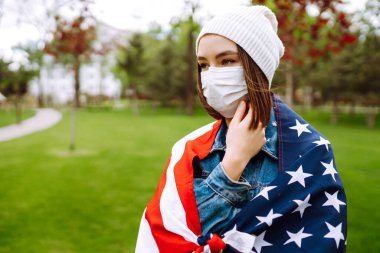 Amerikan bayrağı taşıyan koruyucu maskeli genç bir kız. Amerika 'nın Bağımsızlık Günü. 4 Temmuz. Amerika 'da Coronavirus. Salgının yayılmasını önleme konsepti. 