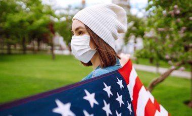 Amerikan bayrağı taşıyan koruyucu maskeli genç bir kız. Amerika 'nın Bağımsızlık Günü. 4 Temmuz. Amerika 'da Coronavirus. Salgının yayılmasını önleme konsepti. 
