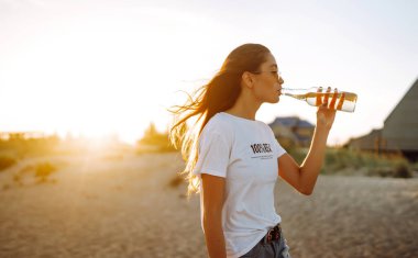 Gün batımında sahilde bira içen güzel kız. Genç bir kadın plaj tatilinde eğleniyor. Yaz, rahatla ve yaşam tarzı kavramı.