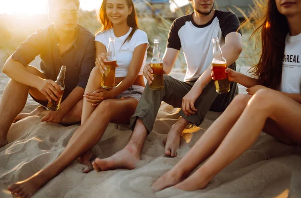 Bir grup genç arkadaş gün batımında sahilde oturup sohbet ediyor ve bira içiyor. Yaz tatili, tatil, rahatlama ve yaşam tarzı kutsallığı.