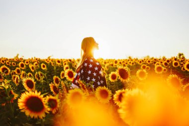 4 Temmuz. Ayçiçeği tarlasında Amerikan bayrağı taşıyan hoş bir kız. Özgürlük. Gün batımı ışığı. Bağımsızlık Günü. Vatansever kavram.