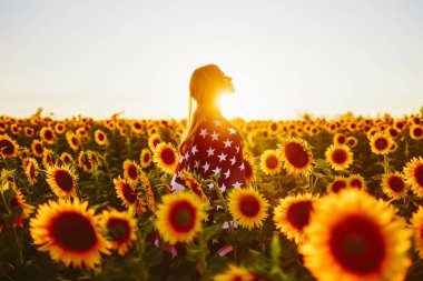 4 Temmuz. Ayçiçeği tarlasında Amerikan bayrağı taşıyan hoş bir kız. Özgürlük. Gün batımı ışığı. Bağımsızlık Günü. Vatansever kavram.