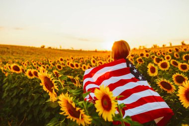 4 Temmuz. Ayçiçeği tarlasında Amerikan bayrağı taşıyan hoş bir kız. Özgürlük. Gün batımı ışığı. Bağımsızlık Günü. Vatansever kavram.
