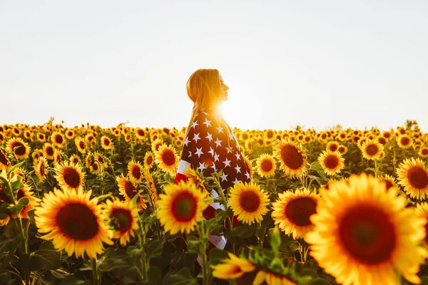 4 Temmuz. Ayçiçeği tarlasında Amerikan bayrağı taşıyan hoş bir kız. Özgürlük. Gün batımı ışığı. Bağımsızlık Günü. Vatansever kavram.