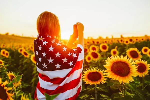 4th of July. Nice girl with the American flag in a sunflower field.Freedom. Sunset light. Independence Day. Patriotic concept.