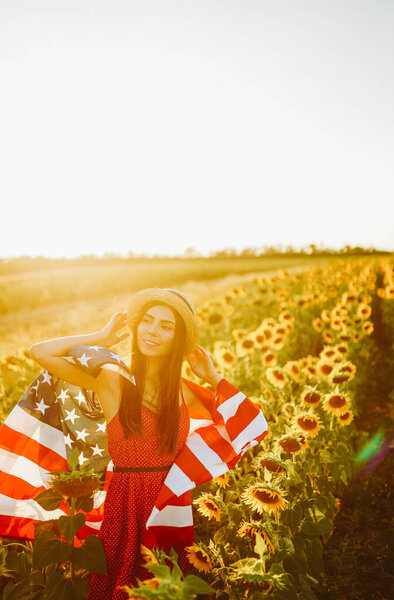 4th of July. Amazing girl in hat with the American flag in a sunflower field. Freedom day. Sunset light. Independence Day. Patriotic concept