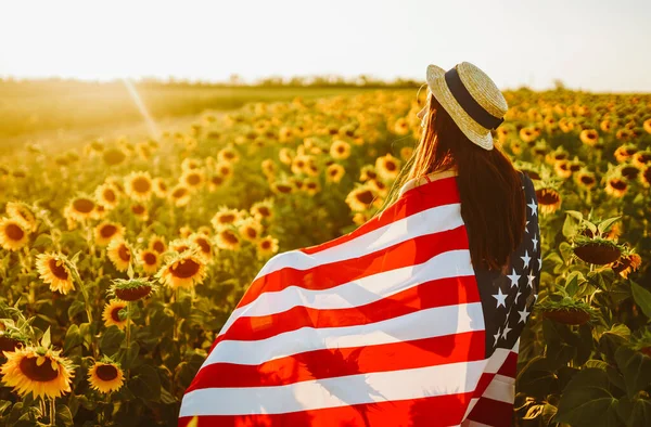 7月4日戴着帽子 戴着美国国旗 站在葵花田里的漂亮姑娘 自由日夕阳西下独立日 爱国观念 — 图库照片