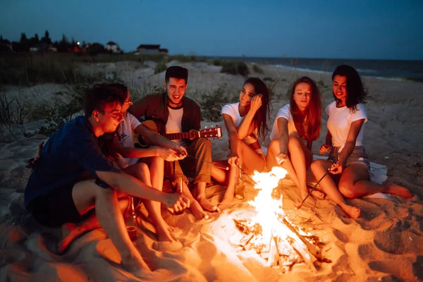 Skupina Mladých Přátel Sedí Pláži Smaží Klobásy Jeden Muž Hraje — Stock fotografie