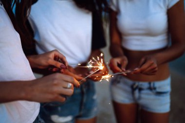 Kumsaldaki genç kızların ellerindeki maytaplar. Plajda maytaplı üç kız eğleniyor. Yaz tatili, tatil, rahatlama ve yaşam tarzı konsepti.