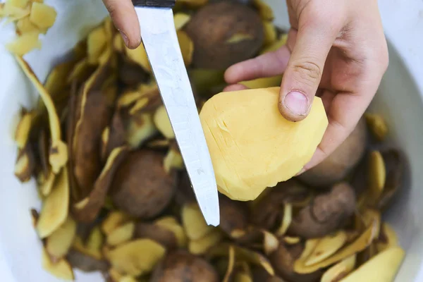 Détail des mains d'enfant pelant la pomme de terre jaune fraîche avec couteau de cuisine . Image En Vente