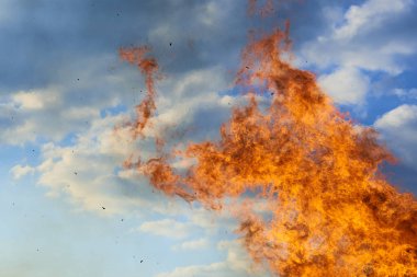 blazing orange red flame of fire against blue day sky 