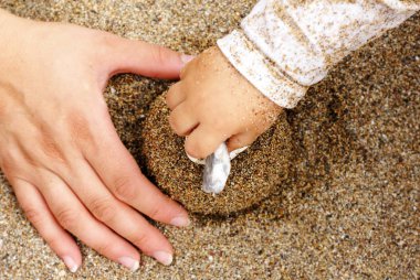 cropped image, mother and child playing with sand on beach 