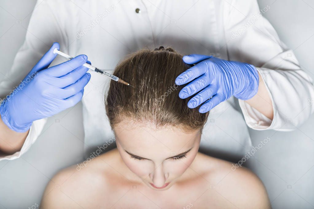 Doctor aesthetician makes head beauty injections to female patient on white background