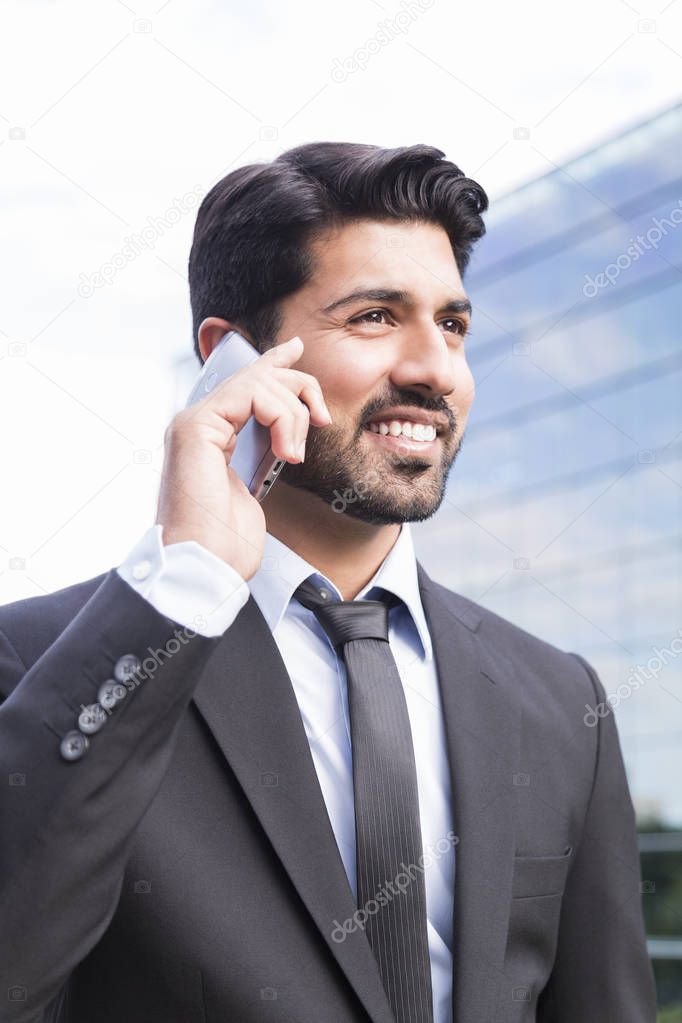 Smiling businessman or worker in suit with phone near office building