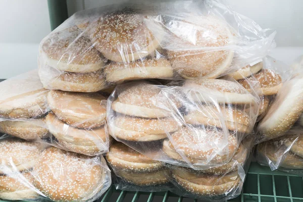Raw frozen buns for burgers of white dough packed in transparent plastic bags.
