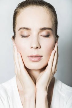 Yüzünde elleri olan güzel sarışın bir kızın portresi.