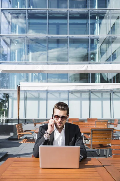 Homem de negócios ou trabalhador de terno preto na mesa e falando ao telefone . — Fotografia de Stock