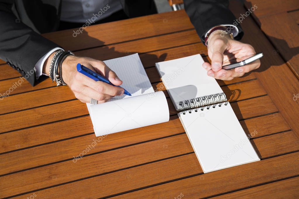 Male businessman or worker in black suit at the table and writing in notebook.