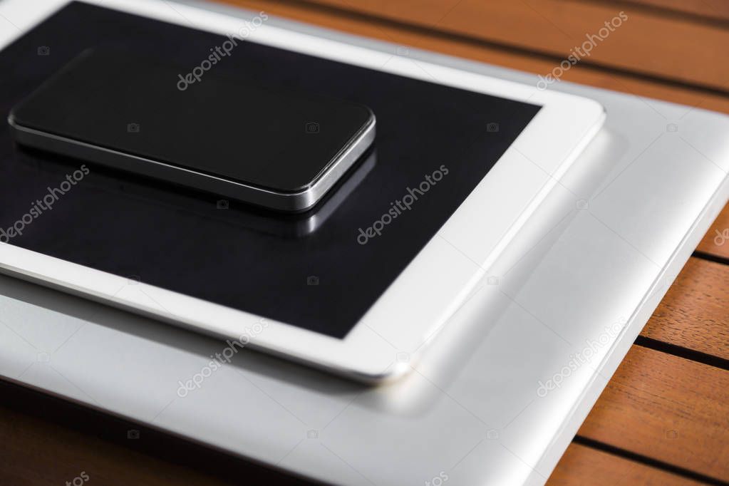 Black mobile phone, tablet, metallic laptop outdoor on an orange wooden table