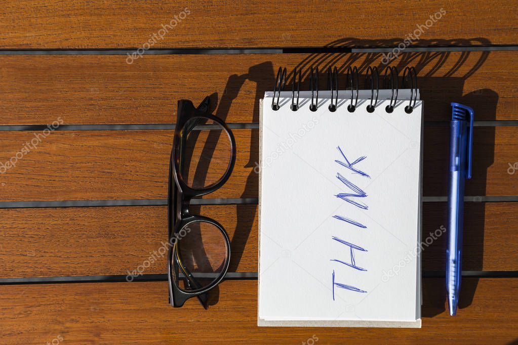 White notepad with think inscription, blue pen and sight glasses