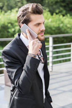 Siyah takım elbise gömlek, bilezik ve Aksesuar ayakta dışında bir kafede ve cep telefonu üzerinde konuşurken elleri ile yakışıklı işçi.