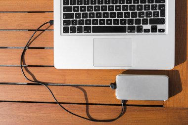 Kafede dışında turuncu ahşap masa üstünde siyah klavye ile metalik dizüstü bilgisayara usb kablo ile bağlı beyaz akıllı telefon ücretleri