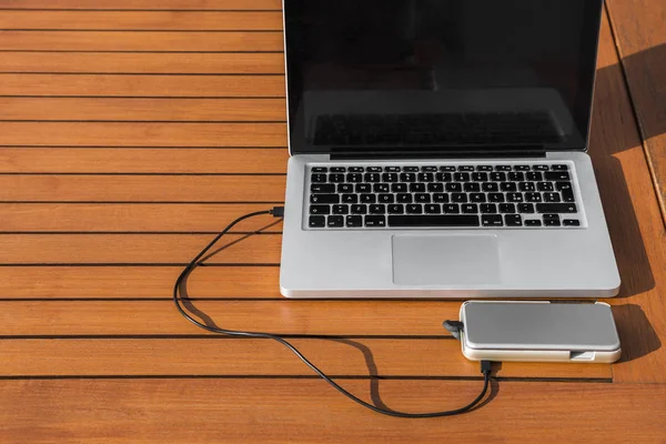 Kafede dışında turuncu ahşap masa üstünde siyah klavye ile metalik dizüstü bilgisayara usb kablo ile bağlı beyaz akıllı telefon ücretleri