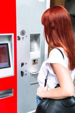 Genç kızıl saçlı kadın, banknotu terminale yerleştiriyor.