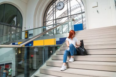 Kız merdivenlerde oturuyor ve çantasında bir şeye bakıyor.