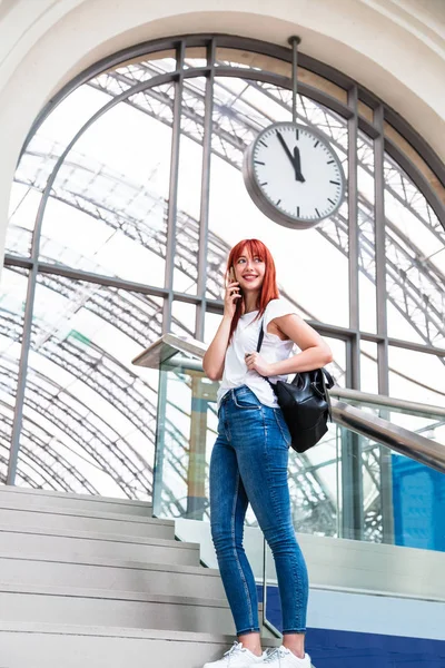 Chica con teléfono inteligente se encuentra bajo un gran reloj de pared —  Fotos de Stock