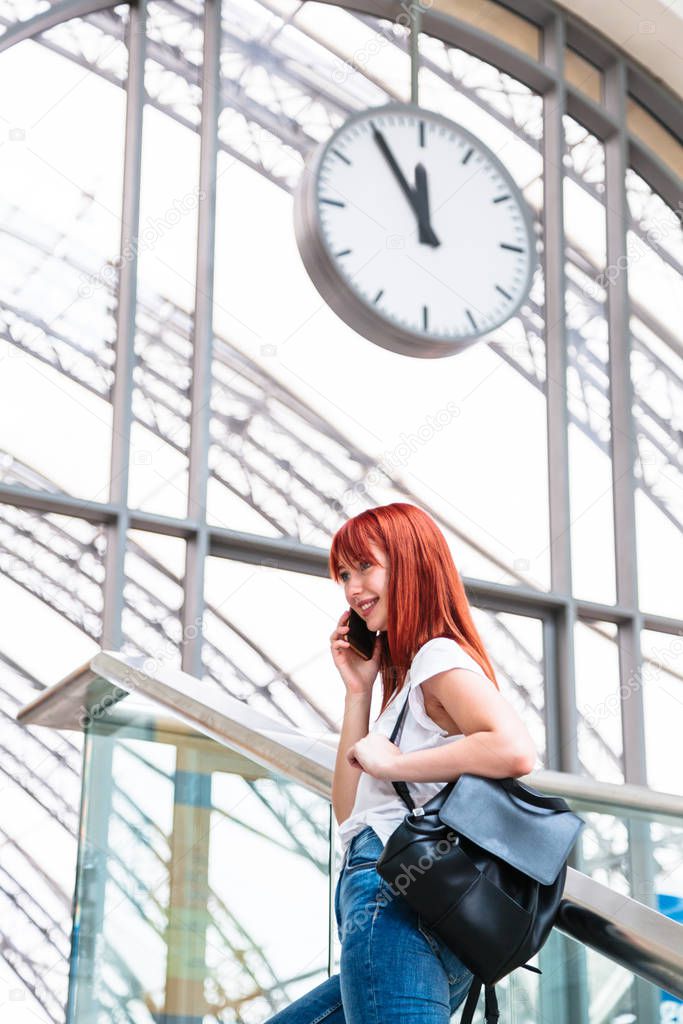 Girl talking on phone on background with wall clock on railway station