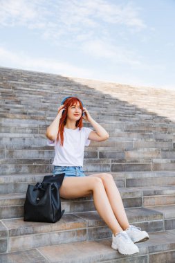 Genç bir kadın merdivenlerde oturmuş müzik dinliyor.