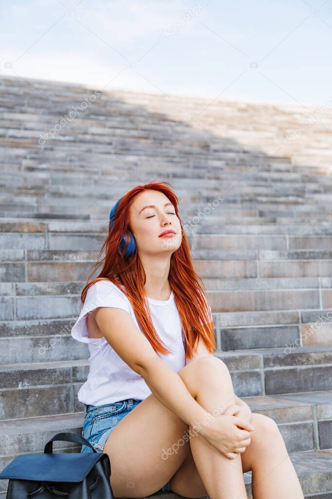 Young girl enjoys sun and music sitting on stairs