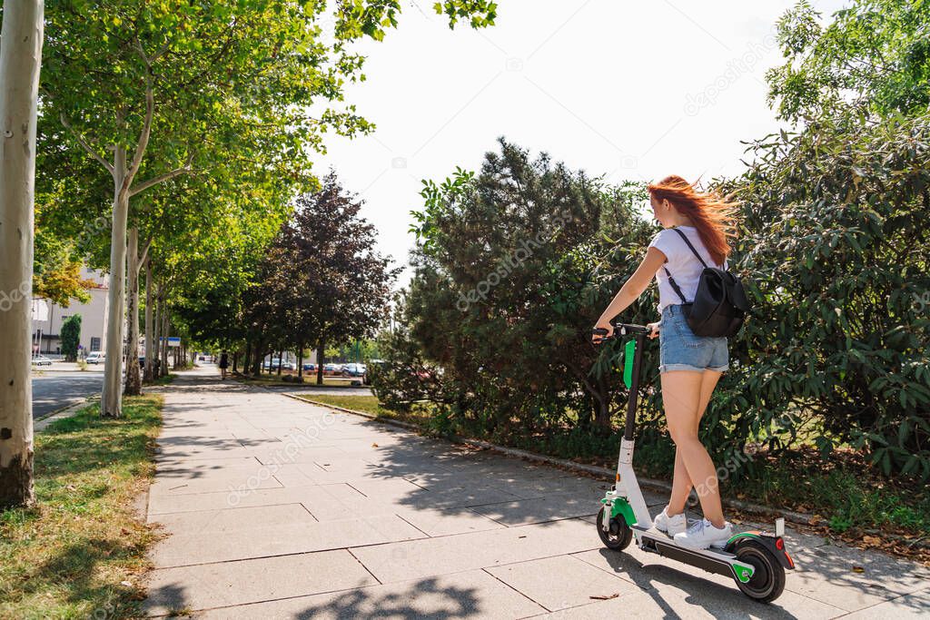 Woman rides on electric scooter along sunny street
