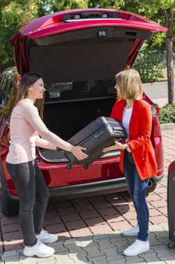 Kız arkadaşının ağır bavulu arabaya koymasına yardım ediyor.