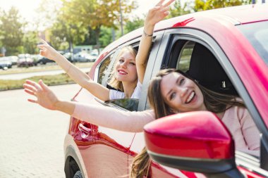 İki genç mutlu kadın arabanın camından sarkıyor.