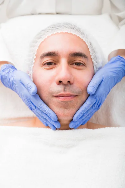 Face of man in disposable cap while beauty massage