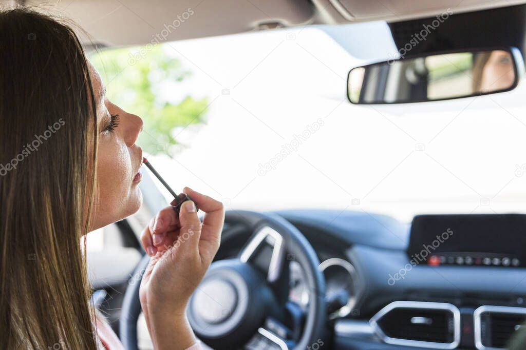 Girl paints lips with gloss looks in mirror in car