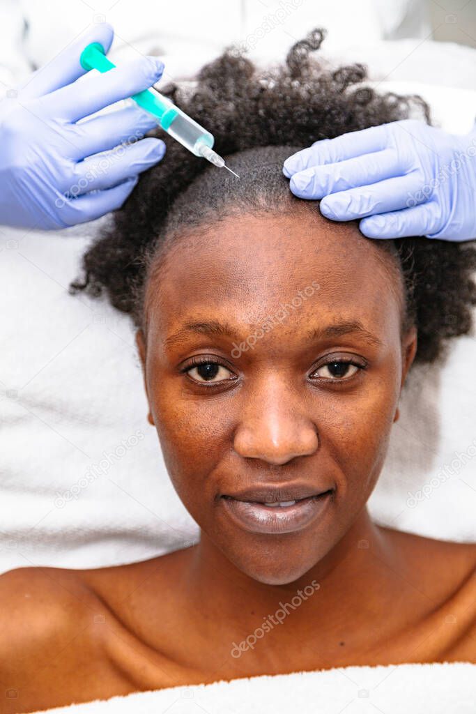 Doctor aesthetician makes head beauty injections to a female african patient