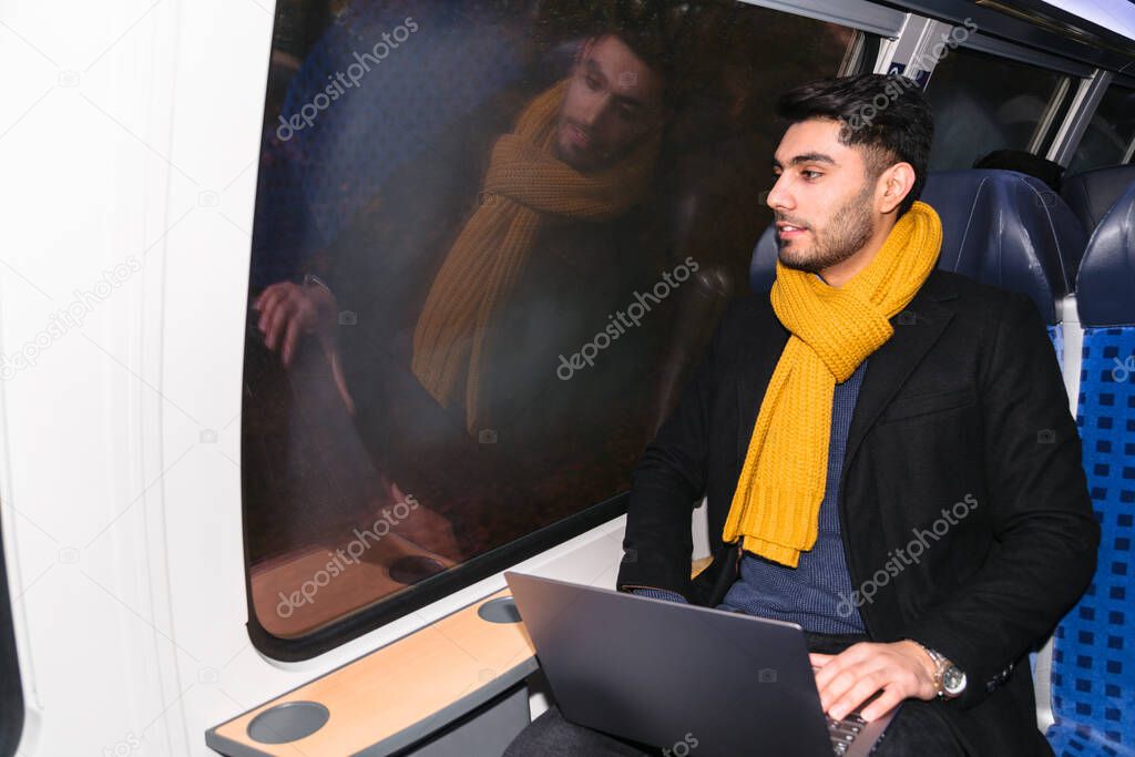 Arab man in train holds laptop and looks at camera