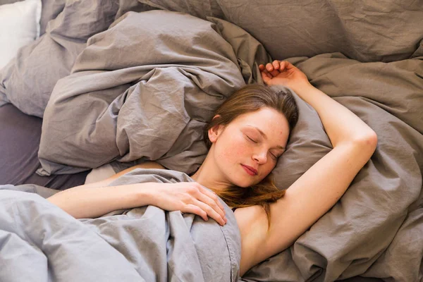 Chica joven duerme sola en el dormitorio en ropa de cama gris —  Fotos de Stock