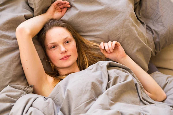 침대에 늘어져 있는 젊은 여자가 아침에 일어났다 — 스톡 사진