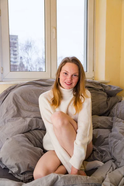 Kazaklı kız pencerenin yanında dizlerine sarılıyor.