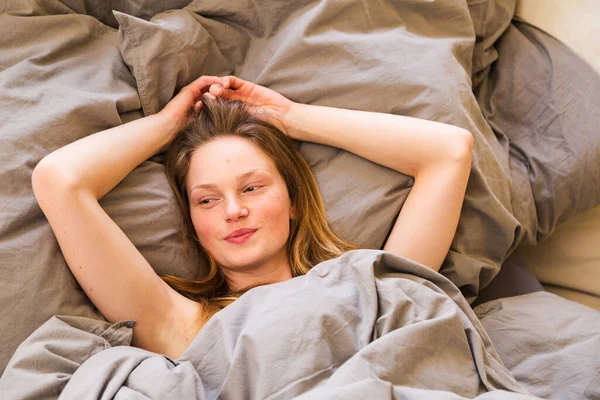 Riéndose despertando chica acostada en la cama bajo las cubiertas —  Fotos de Stock