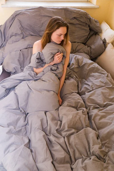 Młoda dziewczyna siedzi sama w łóżku, chowa się w kocu — Zdjęcie stockowe