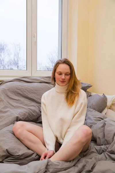 따뜻 한 스웨터를 입은 소녀는 침대에서 연꽃 모양의 자세를 취하고 있다 — 스톡 사진