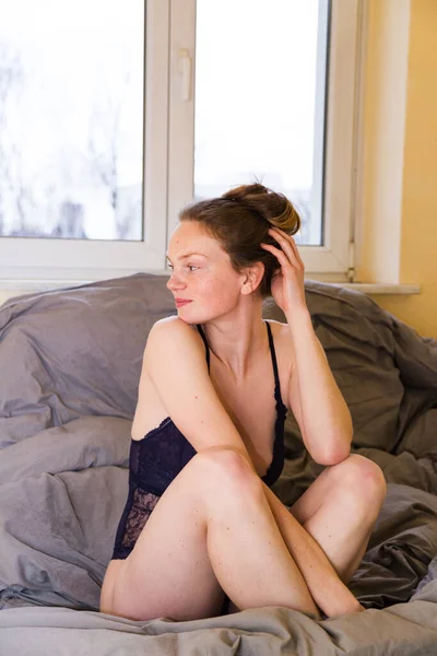 Chica en sujetador se sienta en la cama y descansa la cabeza en la mano —  Fotos de Stock