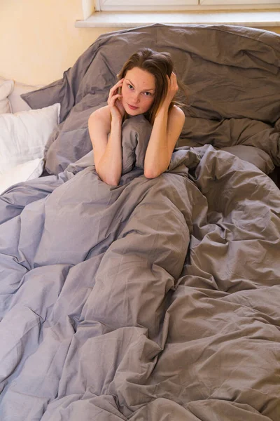 Junges Mädchen sitzt allein im Bett und versteckt sich in Decke — Stockfoto